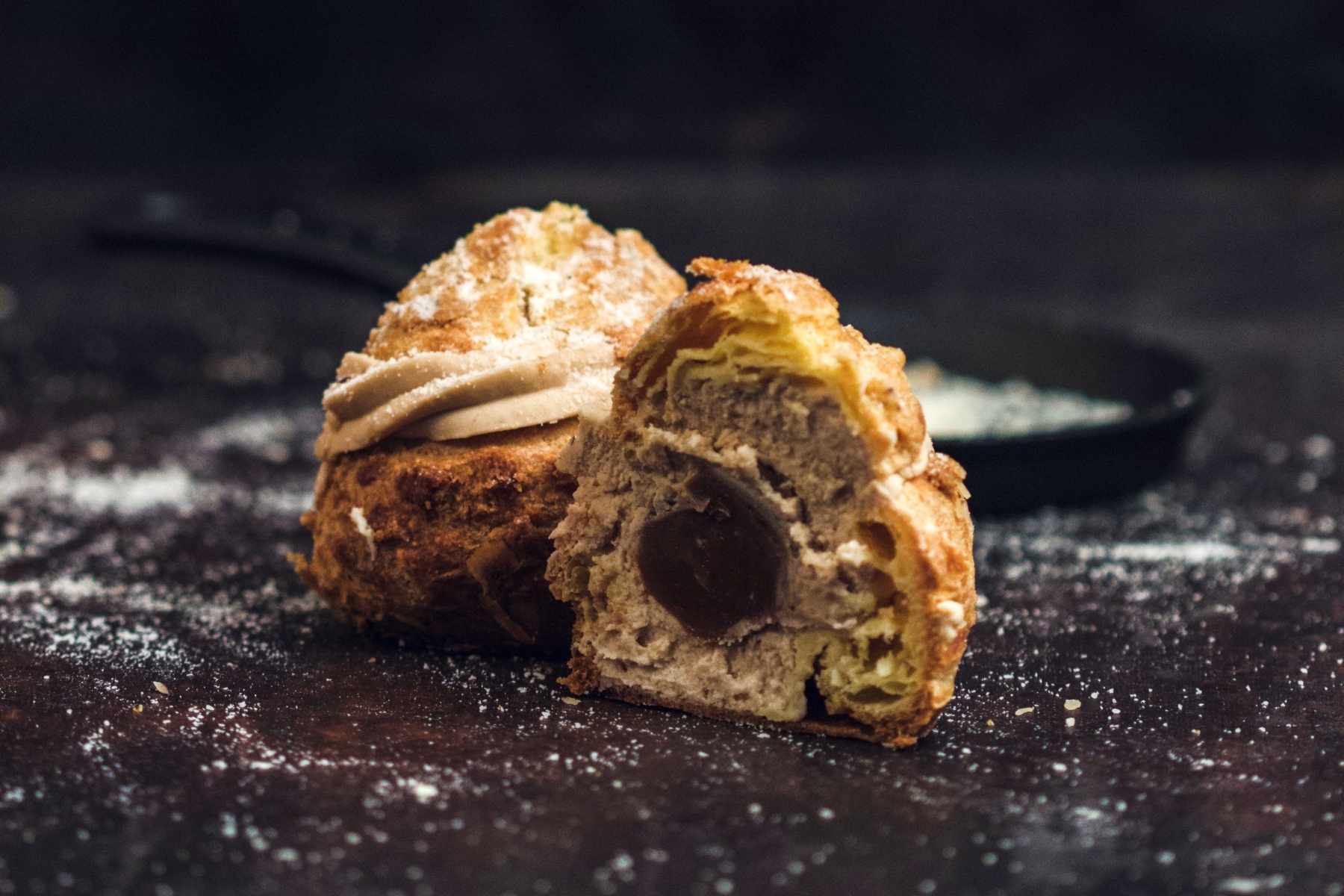 Ein aufgeschnittenes Windbeutelchen mit reichhaltiger Schokoladenfüllung und Zuckerguss auf dunklem Untergrund erinnert an die Genüsse einer Desserttafel zur Weihnachtsfeier.