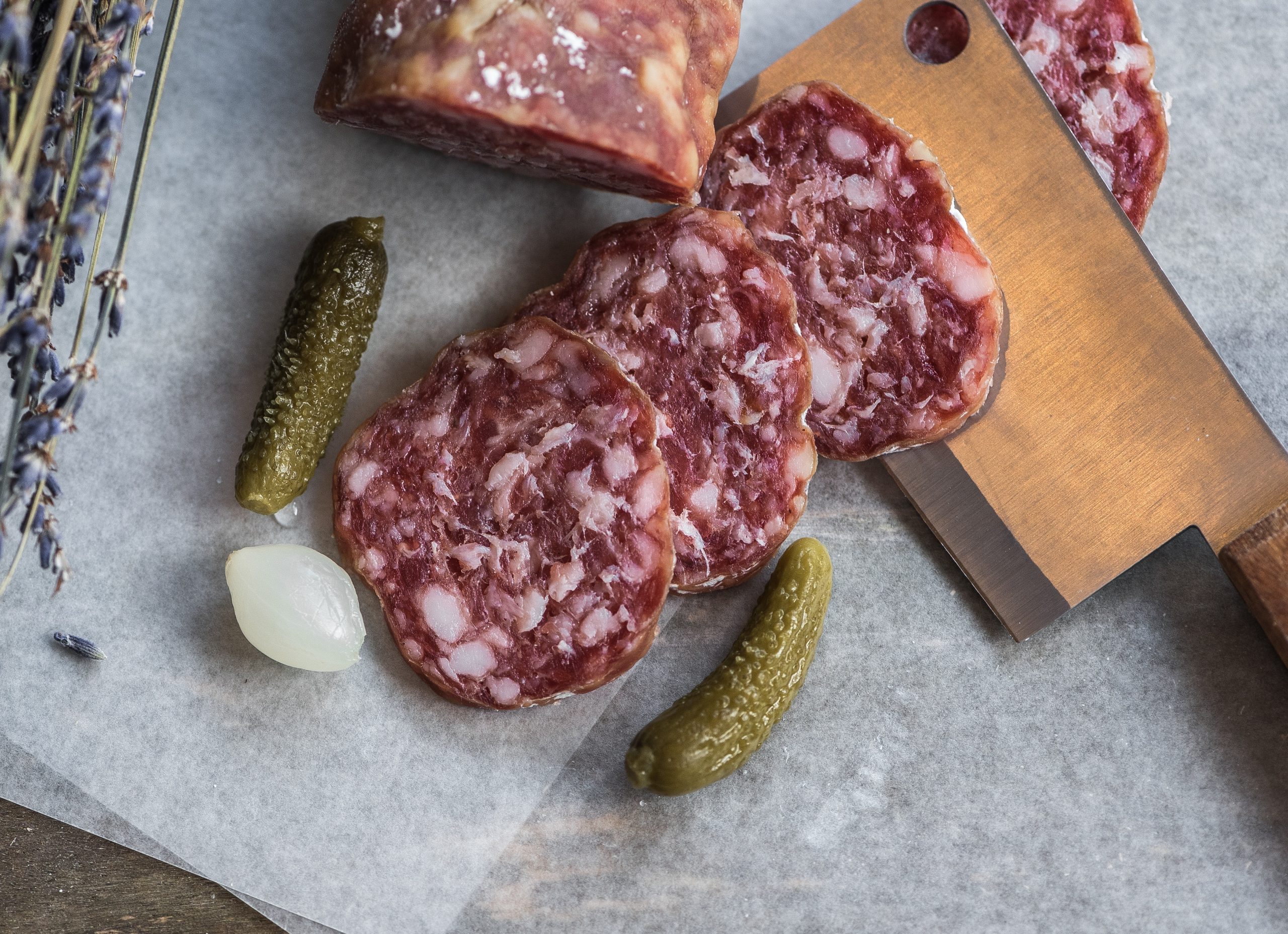 Aufgeschnittene Salami auf einem Schneidebrett mit Gewürzgurken und einer Perlzwiebel, perfekt für Ihr Weihnachtsfeier-Buffet.