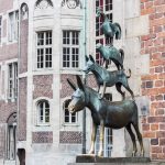 Statue von vier übereinander gestapelten Tieren: Esel, Hund, Katze und Hahn vor einem historischen Backsteingebäude.