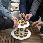 Leute greifen nach geschichteten Desserts mit Fruchtbelag auf einem Etagerentablett.