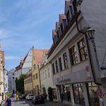 Eine malerische europäische Straße mit farbenfrohen Gebäuden, spazierenden Menschen und einem klaren blauen Himmel.