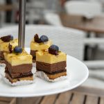 Vierschichtige Mousse-Desserts, garniert mit Blaubeeren auf einem weißen Ständer.