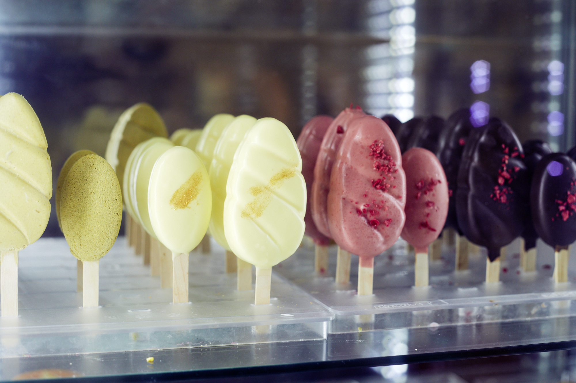 In einer Glasvitrine werden bunt gemischte Eis am Stiel mit unterschiedlichen Geschmacksrichtungen präsentiert und bieten ein Erlebnisgastronomie-Erlebnis für alle, die ein einzigartiges Geschmackserlebnis suchen.