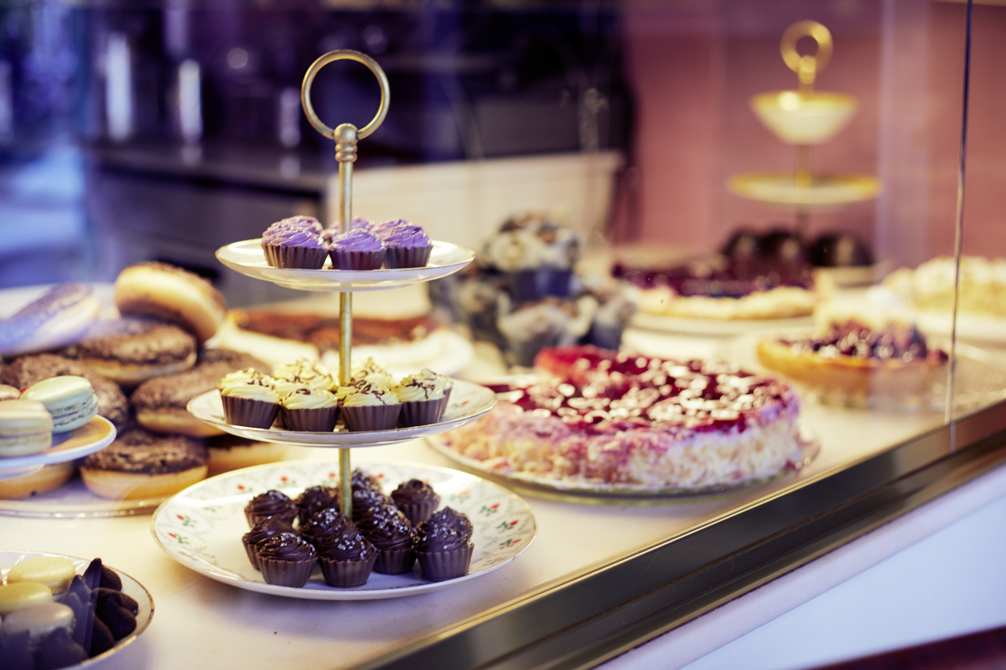 Eine Bäckerei-Auslage mit mehreren Cupcake-Etagen bietet ein wahres Erlebnisgastronomie-Erlebnis mit verschiedenen, hübsch im Hintergrund arrangierten Backwaren.