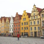 Farbenfrohe historische Gebäude mit Stufengiebeln auf einem Kopfsteinpflasterplatz, auf dem eine einsame Person steht.