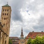 Historische Gebäude mit Steintürmen und einem Kirchturm unter einem bewölkten Himmel.