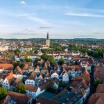 Luftaufnahme der Stadtlandschaft von Osnabrück mit rot gedeckten Gebäuden, historischen Kirchen und üppigem Grün unter einem strahlend blauen Himmel.