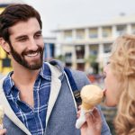 Ein Mann und eine Frau essen im Freien ein Eis, im Hintergrund sind Gebäude zu sehen.