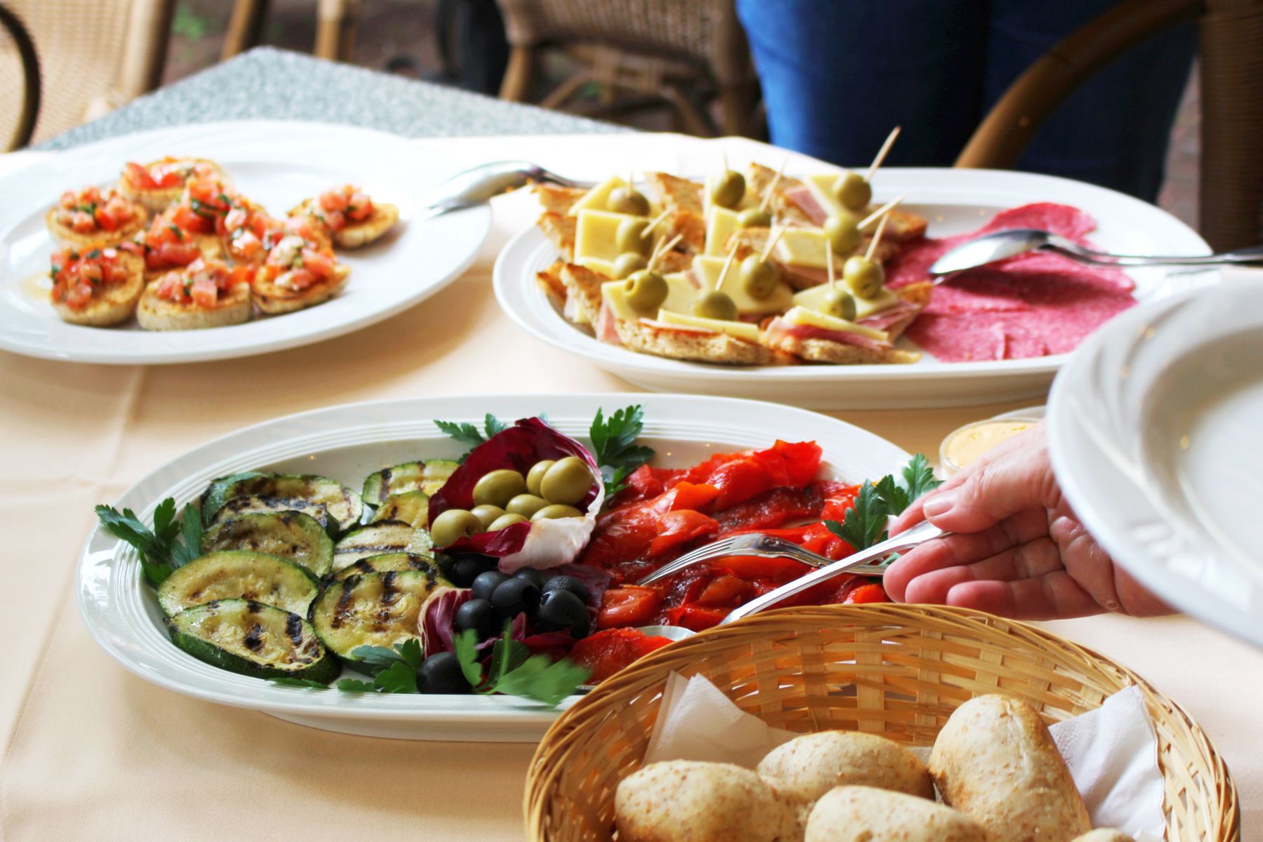 Verschiedene Vorspeisen auf Tellern, darunter gegrilltes Gemüse, Spieße und Bruschetta, mit einer Servierhilfe – eine perfekte Geschenkidee für alle, die kulinarische Genüsse zu schätzen wissen.