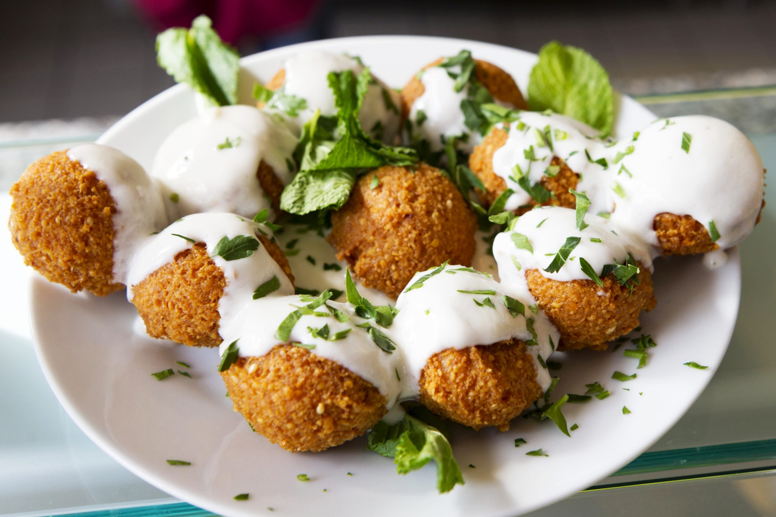 Ein Teller Falafel, beträufelt mit weißer Soße und garniert mit frischen Kräutern, perfekt zum Teilen während eines Junggesellenabschiedsfests.