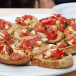 Eine perfekte Vorspeise für einen Junggesellenabschied: Dieser Teller Bruschetta ist mit gewürfelten Tomaten, Käse und Kräutern auf geröstetem Brot belegt.