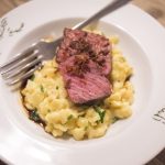 Teller Pasta mit Käse, belegt mit gegrillten Steakscheiben und Garnitur, serviert mit einer Gabel.