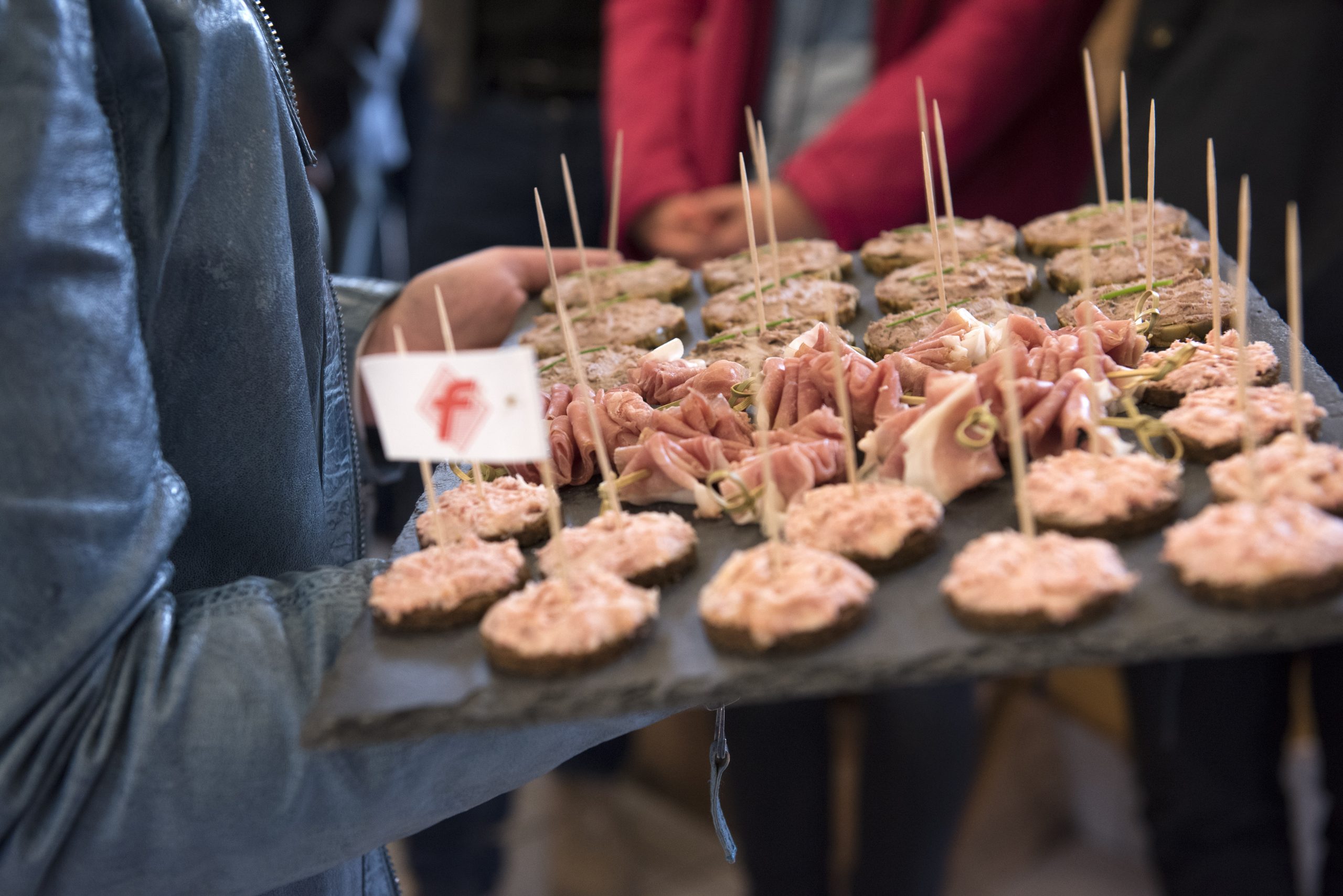 Eine Person hält ein Tablett voller festlicher Appetithäppchen für die Weihnachtsfeier, darunter herzhafte Fleischgerichte und Mini-Sandwiches, die alle sorgfältig mit Zahnstochern bestückt sind.