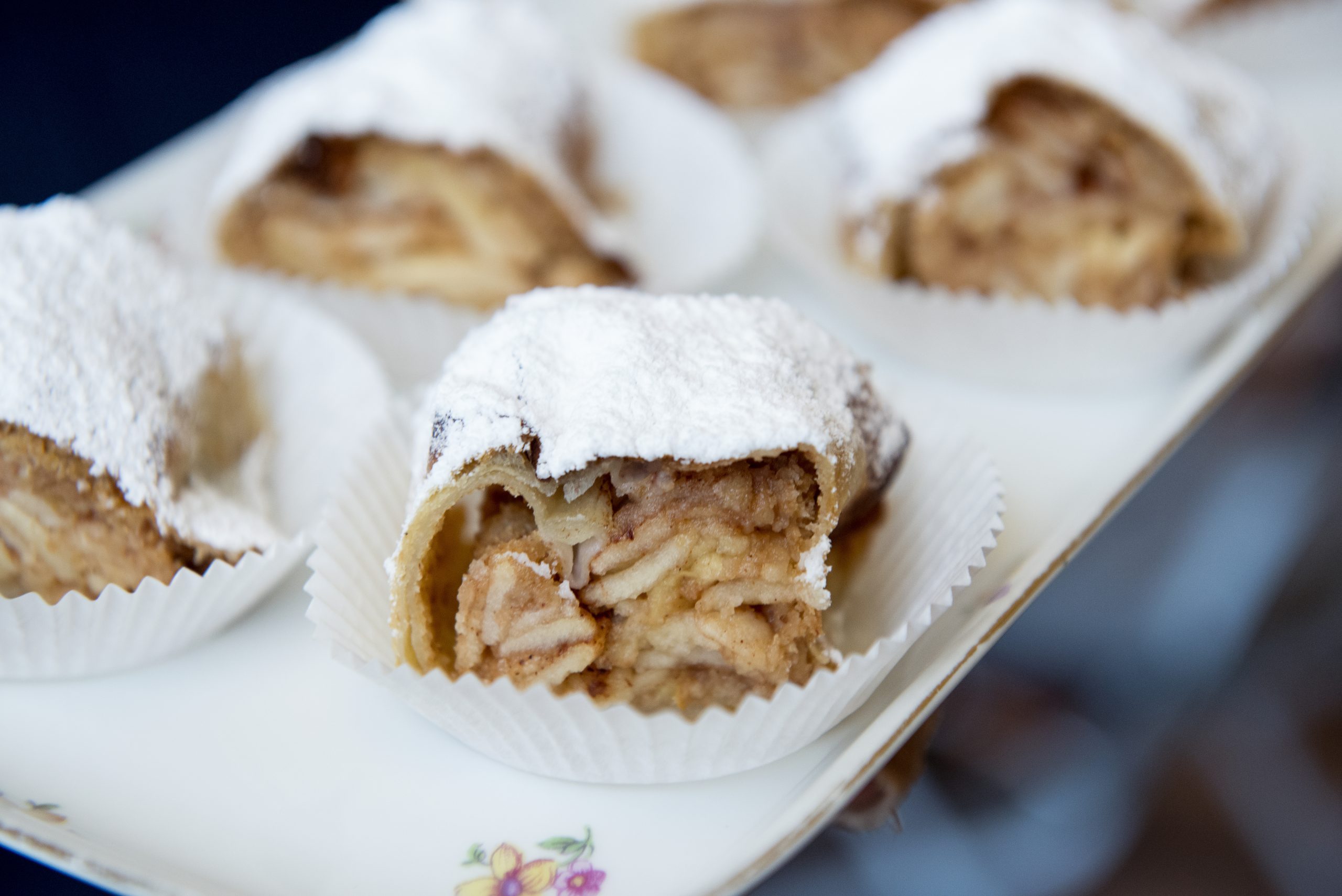 Nahaufnahme von geschnittenem Apfelstrudel, bestäubt mit Puderzucker auf einem dekorativen Tablett, perfekt für eine Weihnachtsfeier.