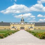 Panoramablick auf das Karlsruher Schloss mit gepflegten Gärten, majestätischen Bäumen und dem malerischen Karlsruher Himmel im Hintergrund.