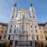 Abtei im Barockstil mit zentralem Innenhof und dekorativem Brunnen unter einem klaren blauen Himmel.