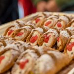 Ein Tablett mit Cannoli, gefüllt mit Sahne und garniert mit roten Kirschen, bestäubt mit Puderzucker.