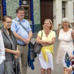 Eine Gruppe von Menschen lächelt und unterhält sich an einem sonnigen Tag vor einem Gebäude.