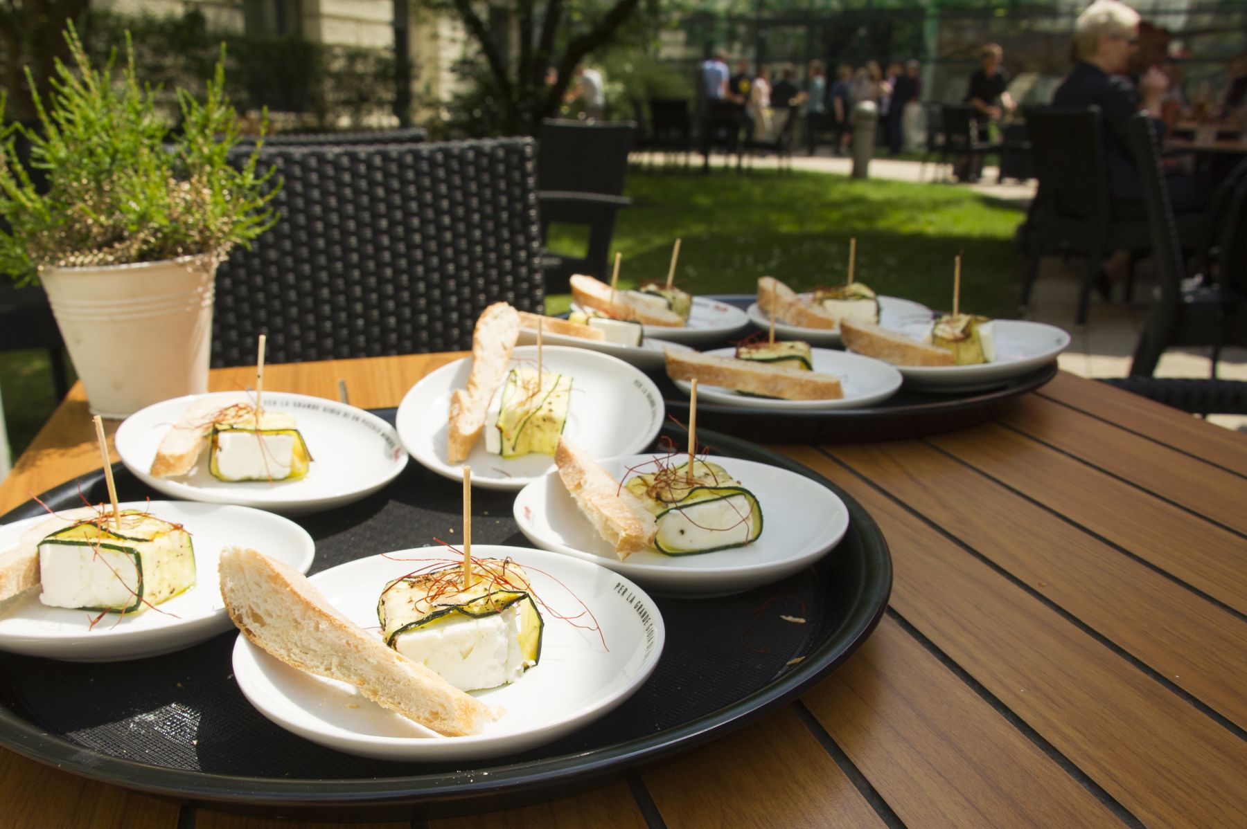 Bei einem charmanten Betriebsausflug stehen Teller mit Brot und Käse, garniert mit Kräutern, elegant auf einem Holztisch in einer einladenden Umgebung im Freien.