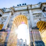 Niedrige Ansicht des Triumphbogens in München mit durchscheinendem Sonnenlicht, umgeben von blauem Himmel.