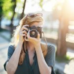 Person im Freien, die mit einer Kamera ein Foto macht, Sonnenlicht im Hintergrund.