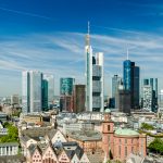 Panoramablick auf die Skyline einer Stadt mit modernen Wolkenkratzern, klarem blauen Himmel und vereinzelten Wolken darüber.