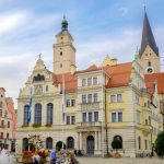 Historischer europäischer Stadtplatz mit Uhrturm, Kirche und Spaziergängern.