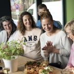 Eine Gruppe von Menschen sitzt lächelnd und plaudernd an einem mit Speisen und Getränken beladenen Tisch in einem gemütlichen Restaurant-Ambiente und teilt wunderbare Erlebnisse.