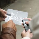 Eine Person hält ein altes Foto in der Hand, eine andere umklammert ein Retro-Handy. Sie stehen auf einem Bürgersteig in der Frankfurter Altstadt und erinnern an Figuren, die sich auf eine Krimi-Rätseltour begeben.