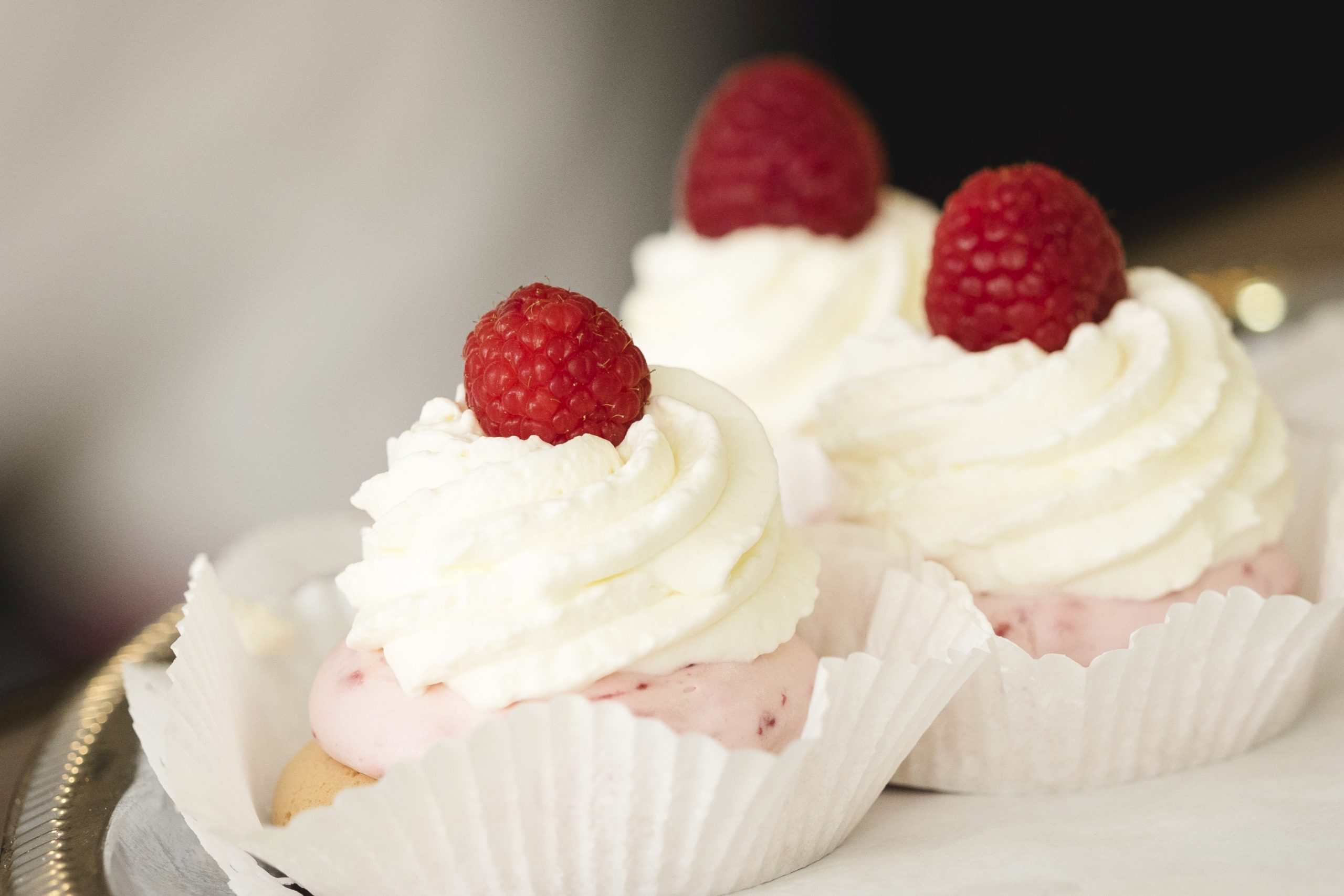 Drei köstliche Cupcakes, garniert mit Schlagsahne und einer frischen Himbeere, perfekt für eine Junggesellenabschiedsfeier, sind elegant auf einem Tablett angerichtet.