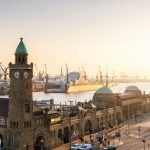 Sonnenuntergang über Hamburgs historischem Hafen mit Türmen und Kränen, die sich gegen den Himmel abzeichnen.