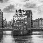 Ein Schwarzweißfoto zeigt die historische Speicherstadt in Hamburg. Umgeben von Kanälen und Brücken ruft es eine GEO EPOCHE-Atmosphäre hervor, über der sich ein wolkiger Himmel erhebt.