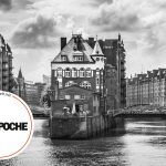 Schwarzweißfoto des historischen Lagerhausviertels mit Kanal, Brücke und Logo in der Ecke.