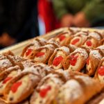 Ein Tablett mit Cannoli, Sahne- und Kirschbelag, mit Puderzucker bestäubt.