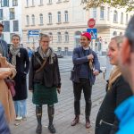 Eine Gruppe von Menschen steht an einem sonnigen Tag auf einem Bürgersteig in der Stadt, unterhält sich und lächelt.