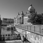 Historisches Gebäude mit einer Kuppel in der Nähe eines Kanals und einem Fahrrad auf einem Zaun; im Hintergrund Bäume und eine Brücke, die an die charmanten Straßen des Leipziger Waldstraßenviertels erinnern. Perfekter Zwischenstopp auf Ihrer Historischen Tour zur Erkundung architektonischer Juwelen.