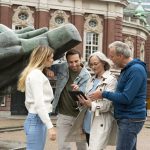 Vier Personen stehen vor einer großen Skulptur in Stuttgart-Mitte und diskutieren angeregt über das auf ihrem Tablet angezeigte Stadtquiz.