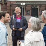 Eine Gruppe von vier Personen unterhält sich fröhlich vor einem historischen Backsteingebäude in einer Kopfsteinpflasterstraße im pulsierenden Berliner Stadtteil Kreuzberg und diskutiert vielleicht über das neueste Stadtquiz.