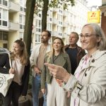 Eine Gruppe lächelnder Menschen auf einem Bürgersteig in einem städtischen Bereich mit Gebäuden und Bäumen, vielleicht eine Firmenveranstaltung, die den Gemeinschaftsgeist stärkt.