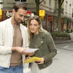 Ein Mann und eine Frau stehen auf einer Stadtstraße und lesen gemeinsam Papiere.