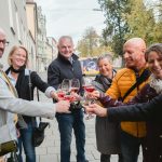 Eine Gruppe von Menschen stößt draußen auf einer Straße mit Weingläsern an.