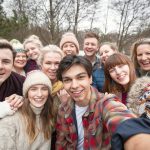 Ein fröhliches Gruppen-Selfie zeigt eine Gruppe lächelnder Freunde an einem kühlen Tag im Freien, alle eingemummelt in gemütliche Winterkleidung und Beanie-Mützen.