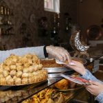 Eine Frau im Hijab reicht einer Kundin in einer Bäckerei über eine Glastheke hinweg Gebäck.