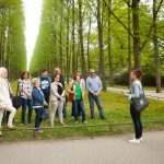 Eine Gruppe von Menschen hört einem Reiseführer in einem von hohen Bäumen und Gras gesäumten Park zu.