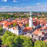 Luftaufnahme der charmanten Stadt Celle mit ihren charakteristischen Gebäuden mit roten Dächern, einem zentralen Kirchturm und üppigem Grün unter einem makellos blauen Himmel.