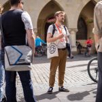 Die Reiseleiterin sprach begeistert mit der Touristengruppe, die sich im Kopfsteinpflasterhof versammelt hatte, umgeben von Fahrrädern und einem gewölbten Gebäude. Wie sie betonte, war dies einer der Höhepunkte unserer Historischen Tour durch die Altstadt, nur einen Steinwurf vom berühmten Münster entfernt.