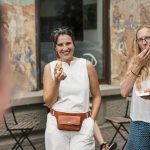 Frauen genießen eine Mahlzeit im Freien; eine lächelt mit einem Sandwich, eine andere bedeckt beim Essen ihren Mund.