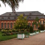 Historisches Gebäude mit Bogenfenstern in einer Gartenanlage. Ein von Grün gesäumter Weg führt zum Eingang.