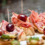 Eine gemütliche Nahaufnahme von aufgespießten Brothäppchen zu Hause, garniert mit herzhaftem Prosciutto und saftigen roten Trauben.