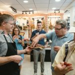 Menschen probieren in einem Feinkostladen Speisen und Weine. Im Hintergrund sind verschiedene Produkte ausgestellt.